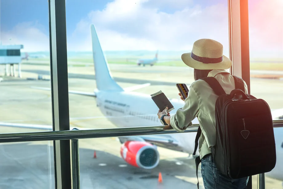 Person scrolling the smartphone while looking out the airport window