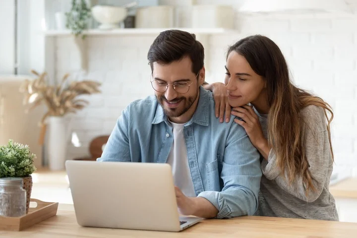 A couple happily sitting by the laptop